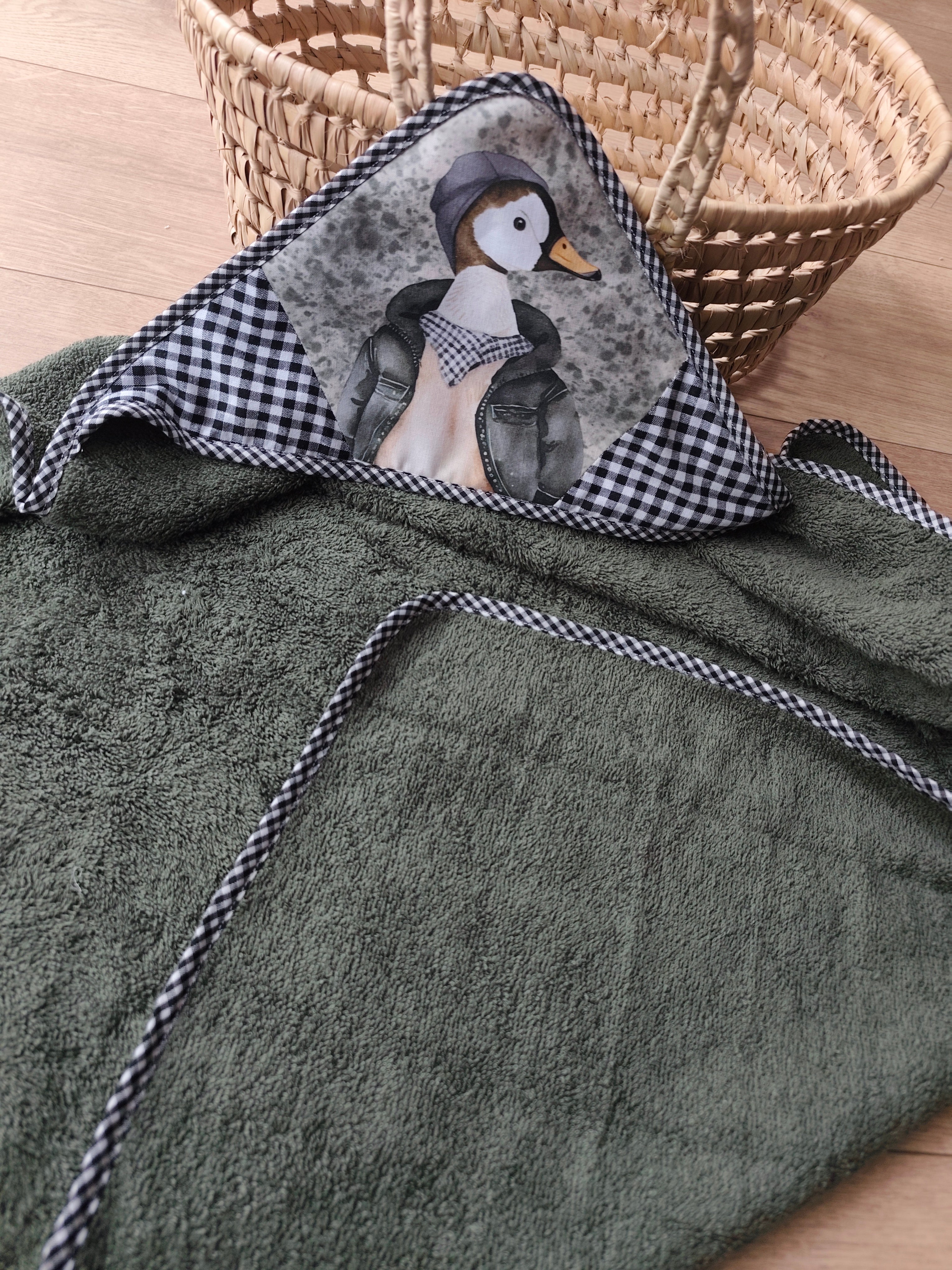 Cape de bain bébé de la collection Gaspard le Canard réalisée en éponge de coton kaki avec capuche en coton imprimé et finitions biais vichy, idéale pour envelopper bébé de douceur après le bain. Blanche & Noé